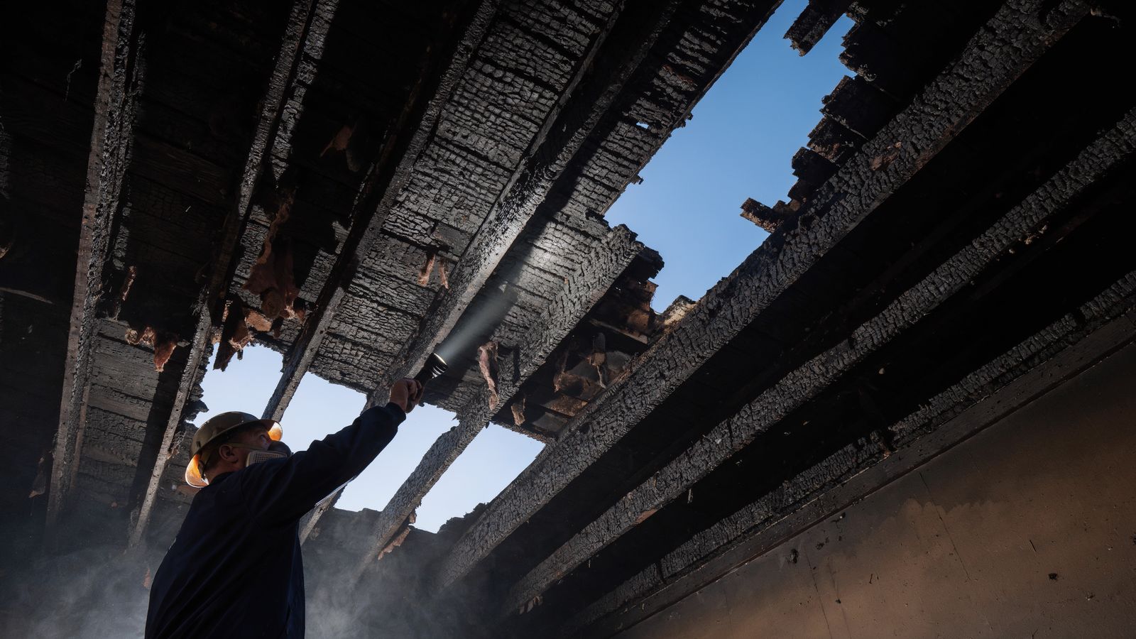 Restoration technician inspecting charred roof rafters with a flashlight inside a fire damaged home
