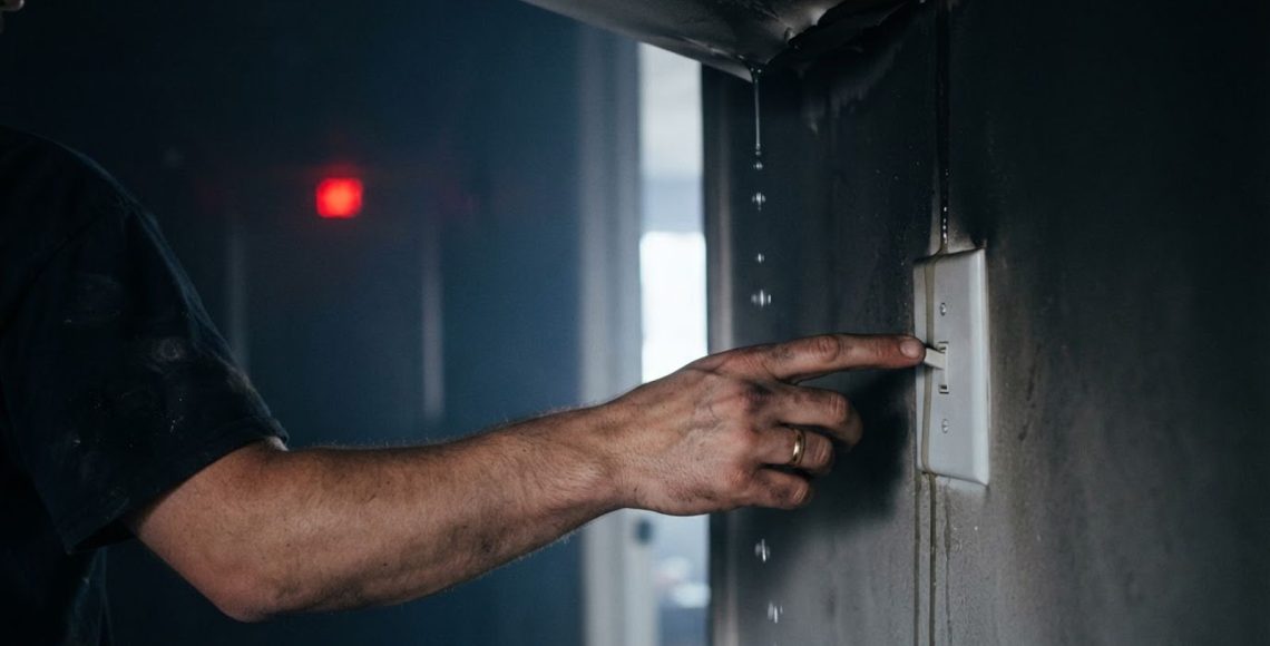Homeowner's hand reaching for a light switch on a soot covered wall with water dripping nearby